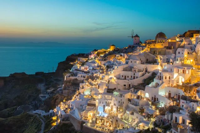 The white houses of Oia, Santorini, lit up at dusk above the sea