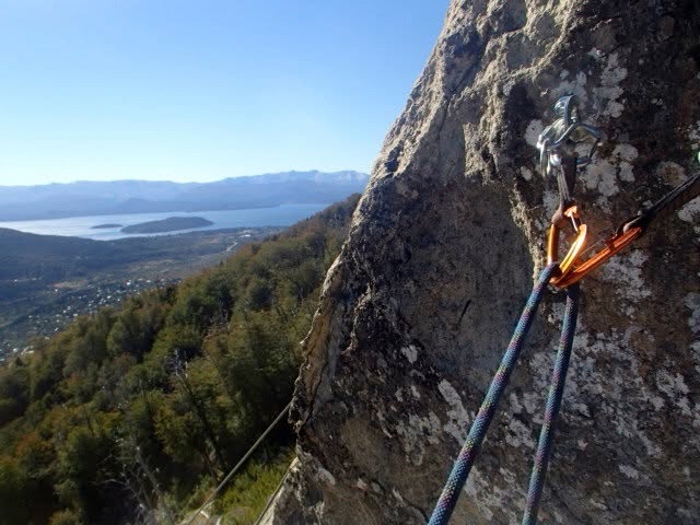 A climbing rope clipped to a bolt on a granite wall high above a forested valley and a lake in Patagonia