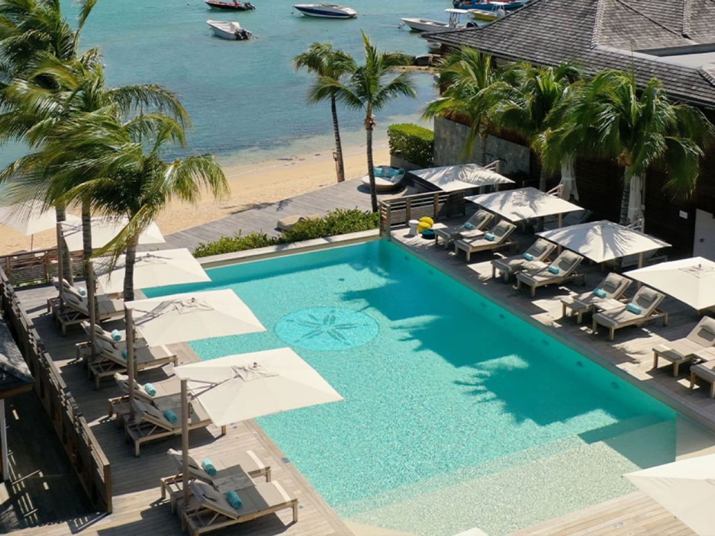 A turquoise pool, palms and a boat-filled bay at Le Barthélemy Hotel & Spa, St. Barths