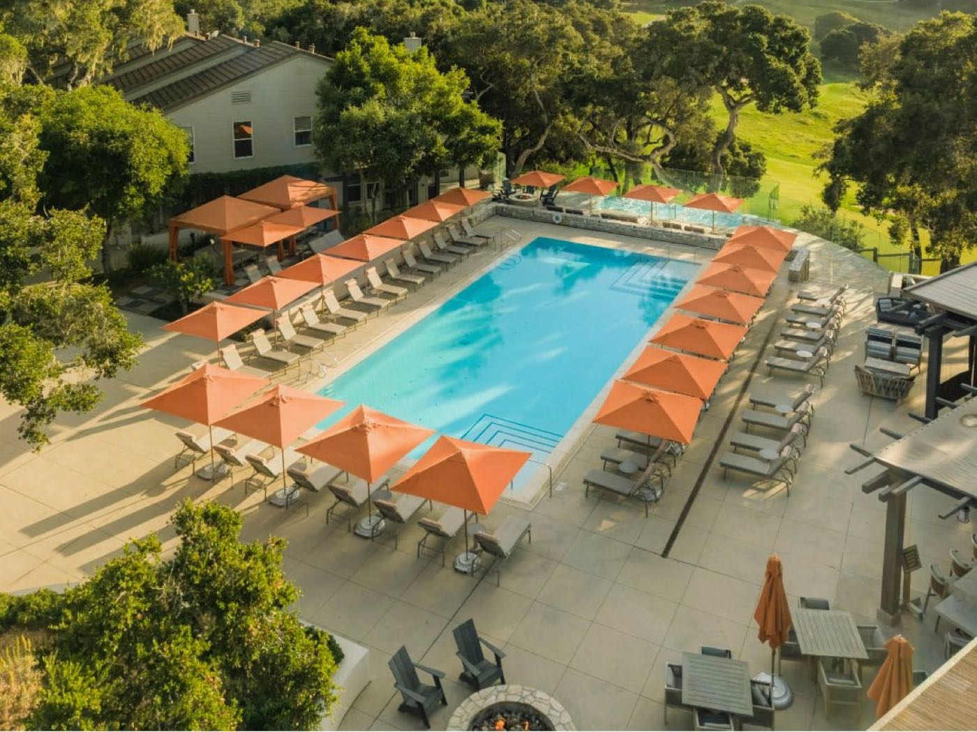 A resort pool with orange umbrellas below green hills at Carmel Valley Ranch, California