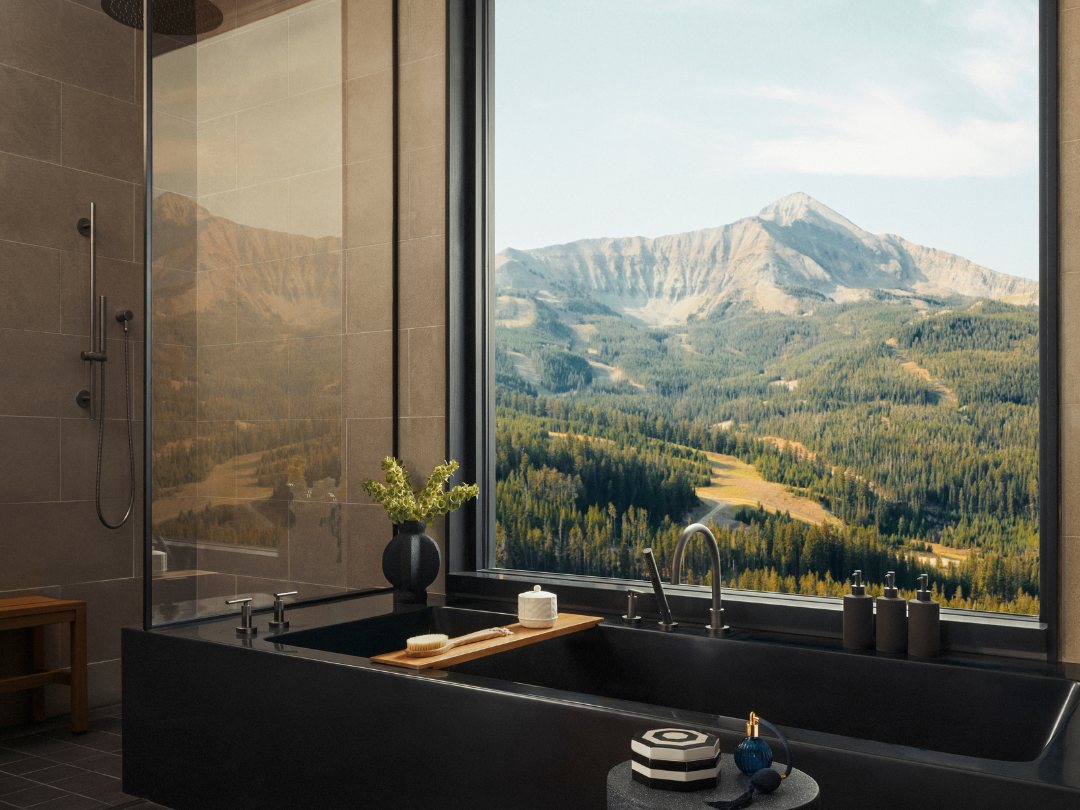A stone bathtub beside a floor-to-ceiling window looking out at a mountain peak at One&Only Moonlight Basin