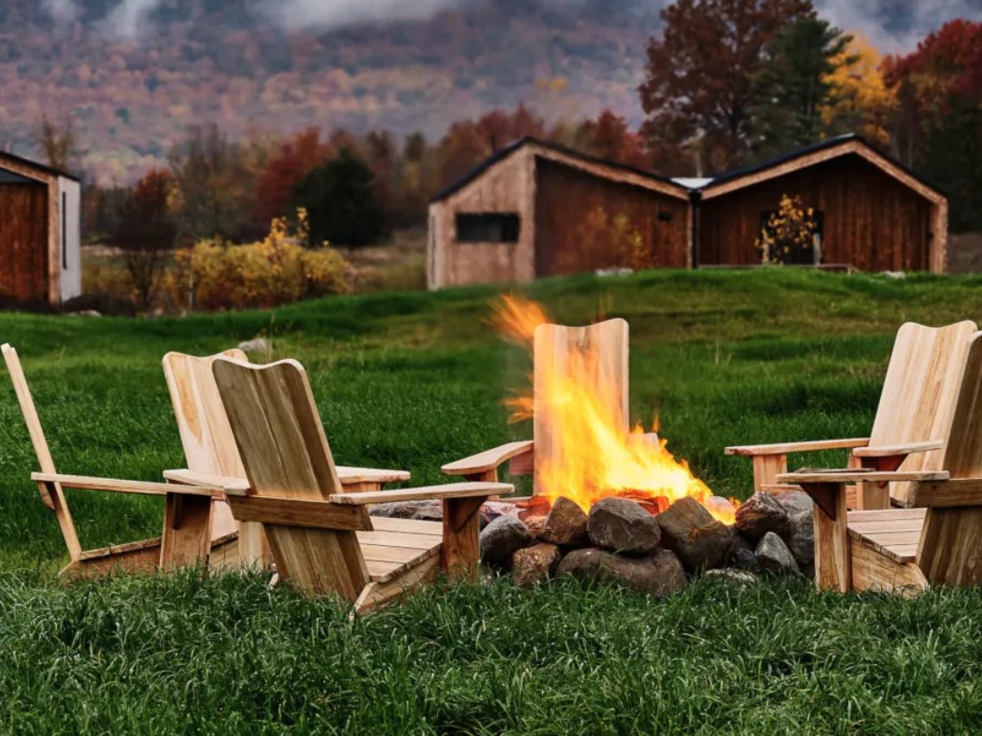 Wooden chairs around a fire pit in front of cabins and misty autumn hills at Wildflower Farms, New York