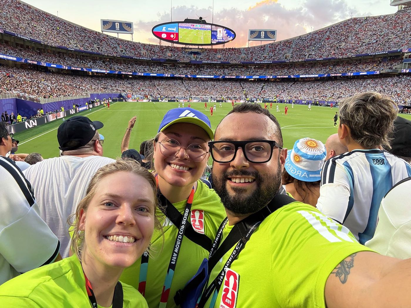 Emily and two fellow volunteers in neon-green uniforms taking a selfie in the stands at Arrowhead